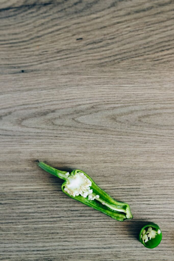 Freshly sliced green chili pepper on wooden surface with seeds visible.