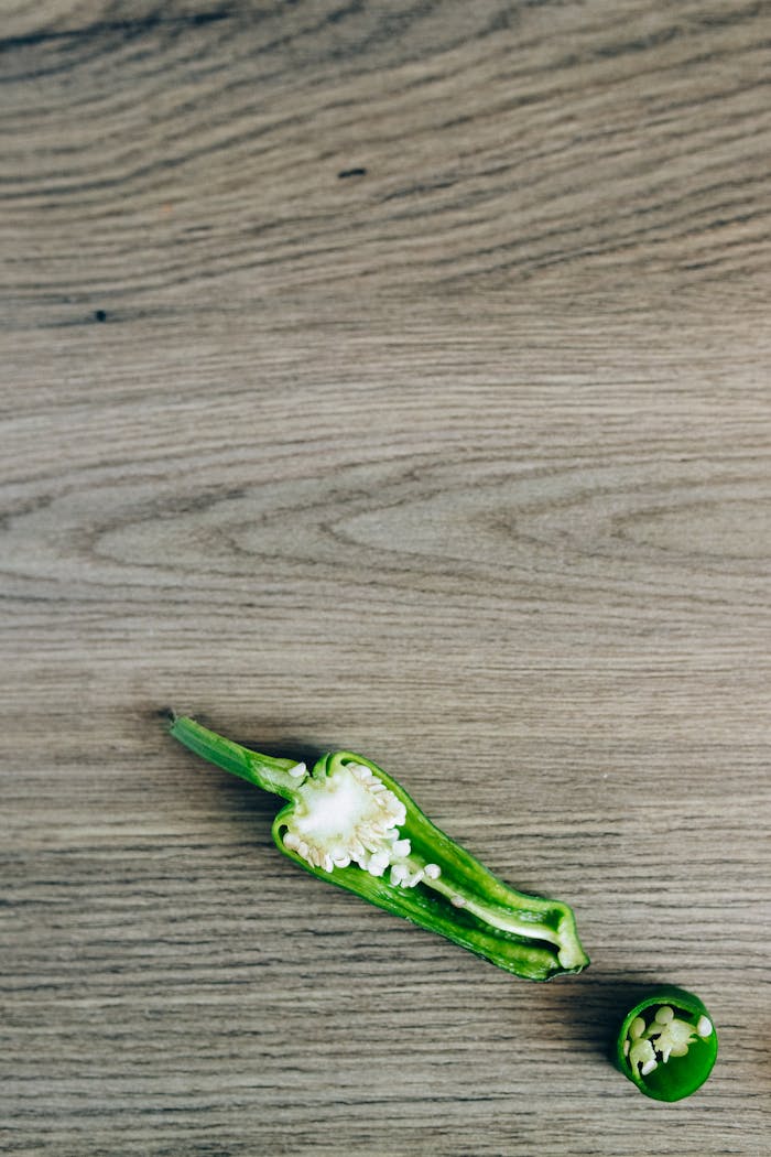 Freshly sliced green chili pepper on wooden surface with seeds visible.