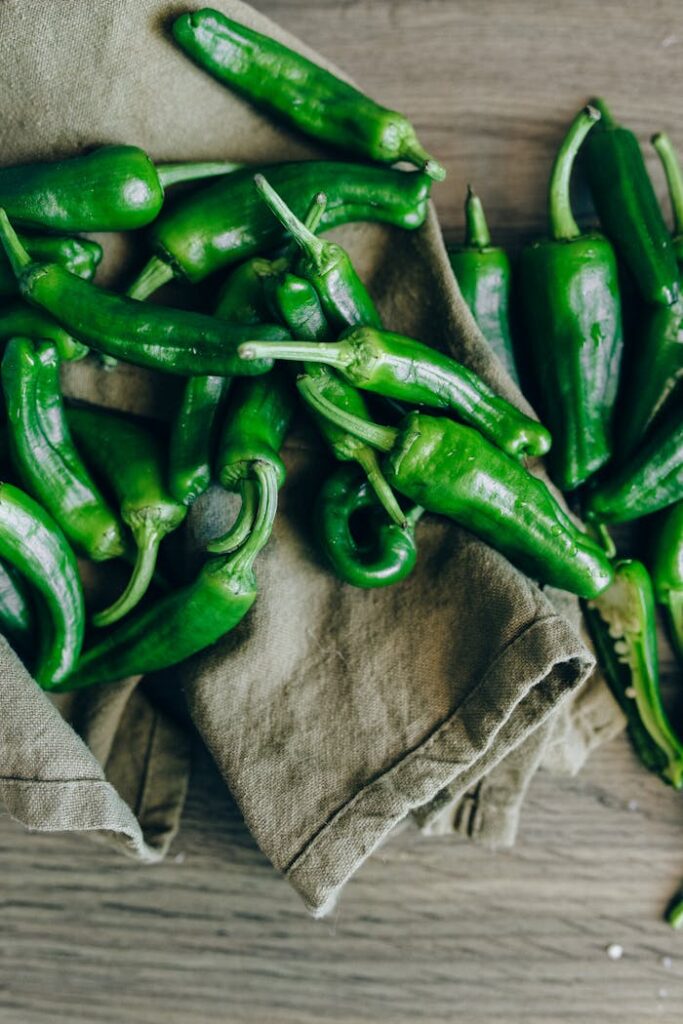 Fresh green chili peppers on cloth over a wooden surface, showcasing raw spicy ingredients.